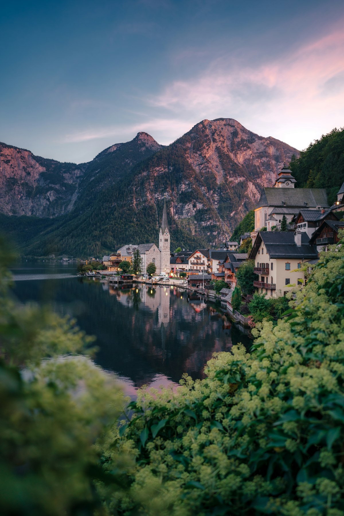 The village of Hallstatt with its church spire reflected in the lake below the mountains at dusk